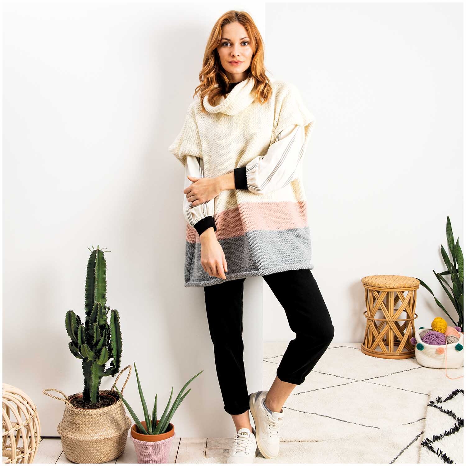 Essentials Mega Wool chunky Pullover in Creme, getragen von einer Frau, umgeben von Pflanzen und Dekor.