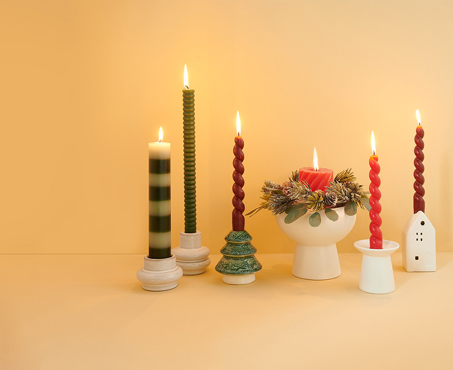 Sechs verschiedene weihnachtliche Kerzenständer mit unterschiedlichen Stab- und Stumpenkerzen. Fotosetting gelber Hintergrund.