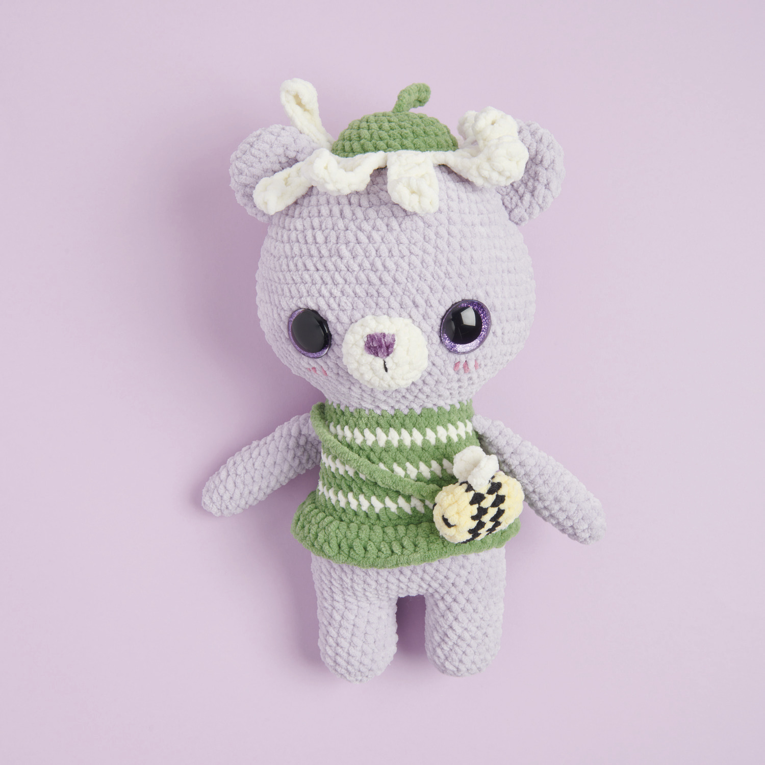 Häkelset Flower Lover Bear Modell 07: Ein lila gehäkelter Bär mit grünem gestreiftem Outfit und Blumenmütze.