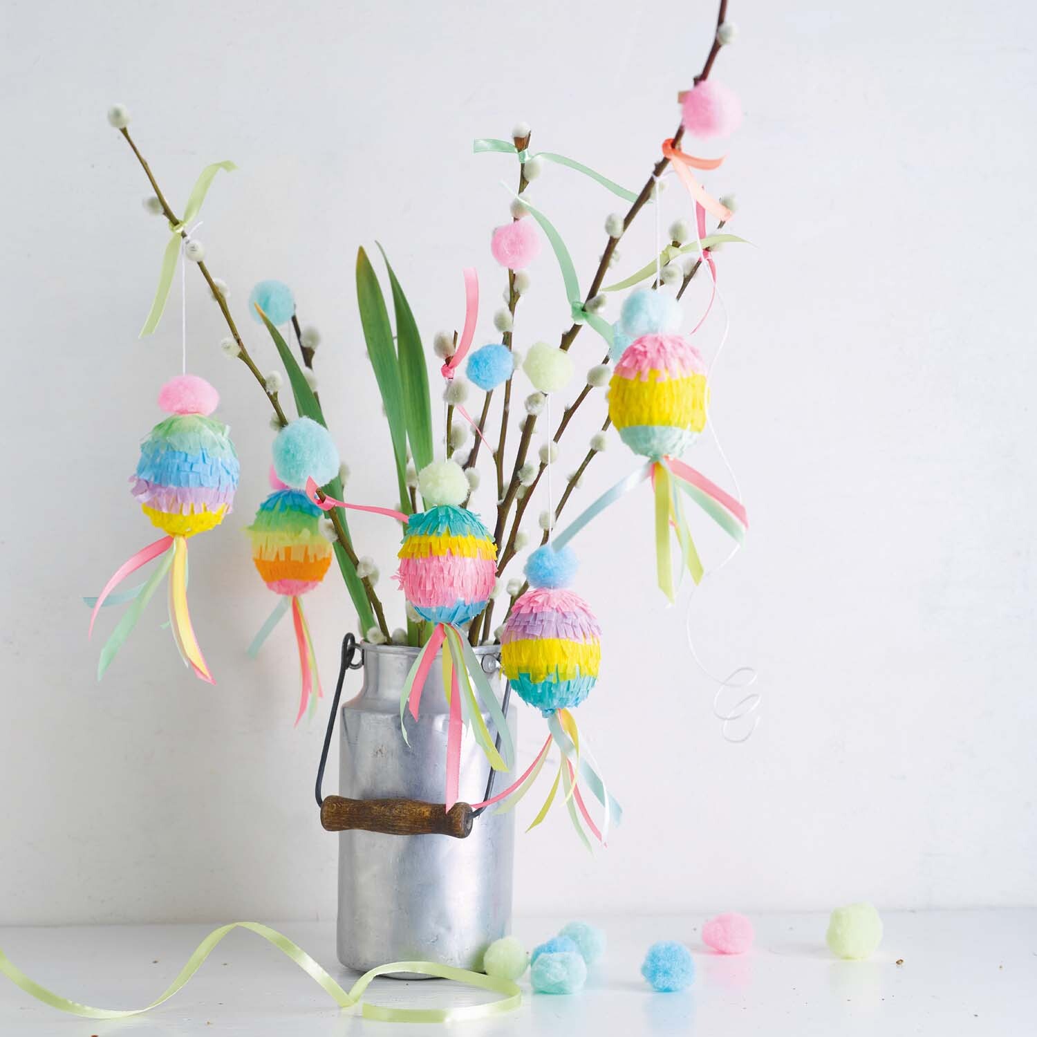 Bastelanleitung Ostereier-Pinata: Bunte Pinatas in Pastellfarben hängen an Zweigen in einem Metalltopf.
