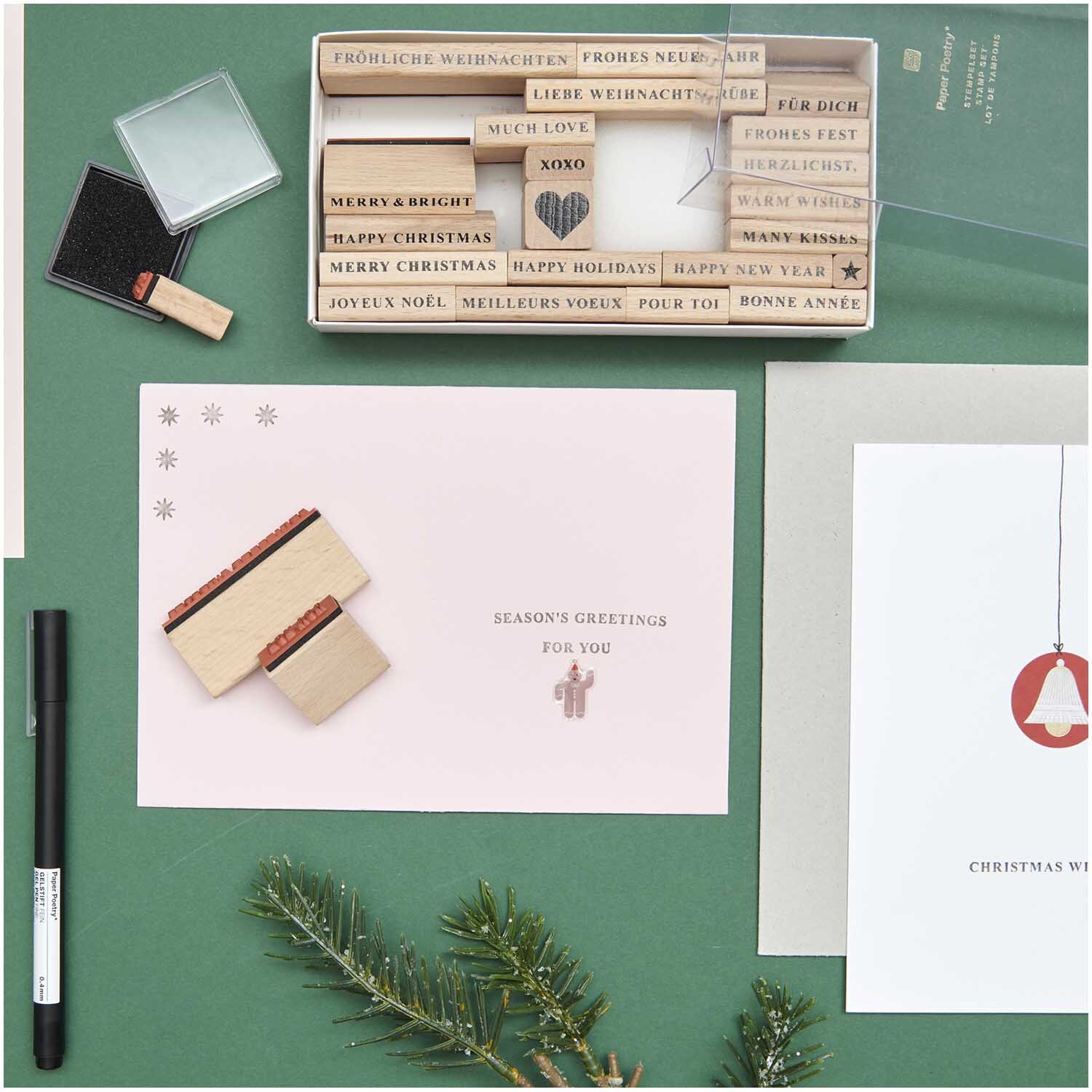 Paper Poetry XL Stempelset Merry Christmas Typewriter, 27-teilig, auf grünem Hintergrund mit Weihnachtskarten und Tannenzweig.