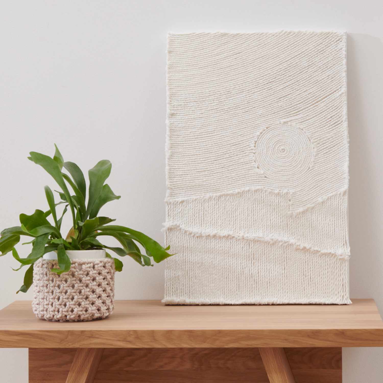 Anleitung 3D-Textil-Art: Ein weißes, strukturiertes Textilkunstwerk auf Holzregal mit Pflanze.