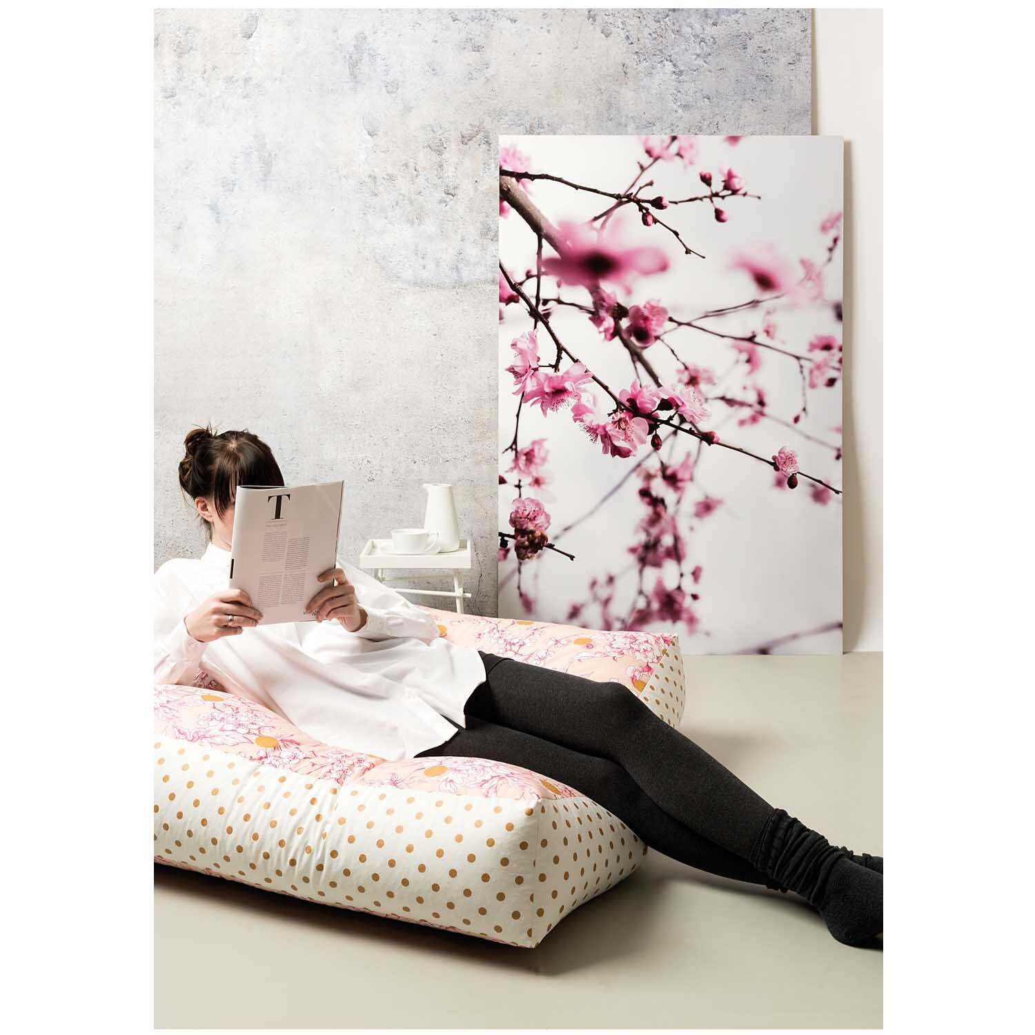 Stoff Punkte weiß-gold 50x140cm von Rico Design: Frau liest auf gepunktetem Stoffbett vor Kirschblütenbild.