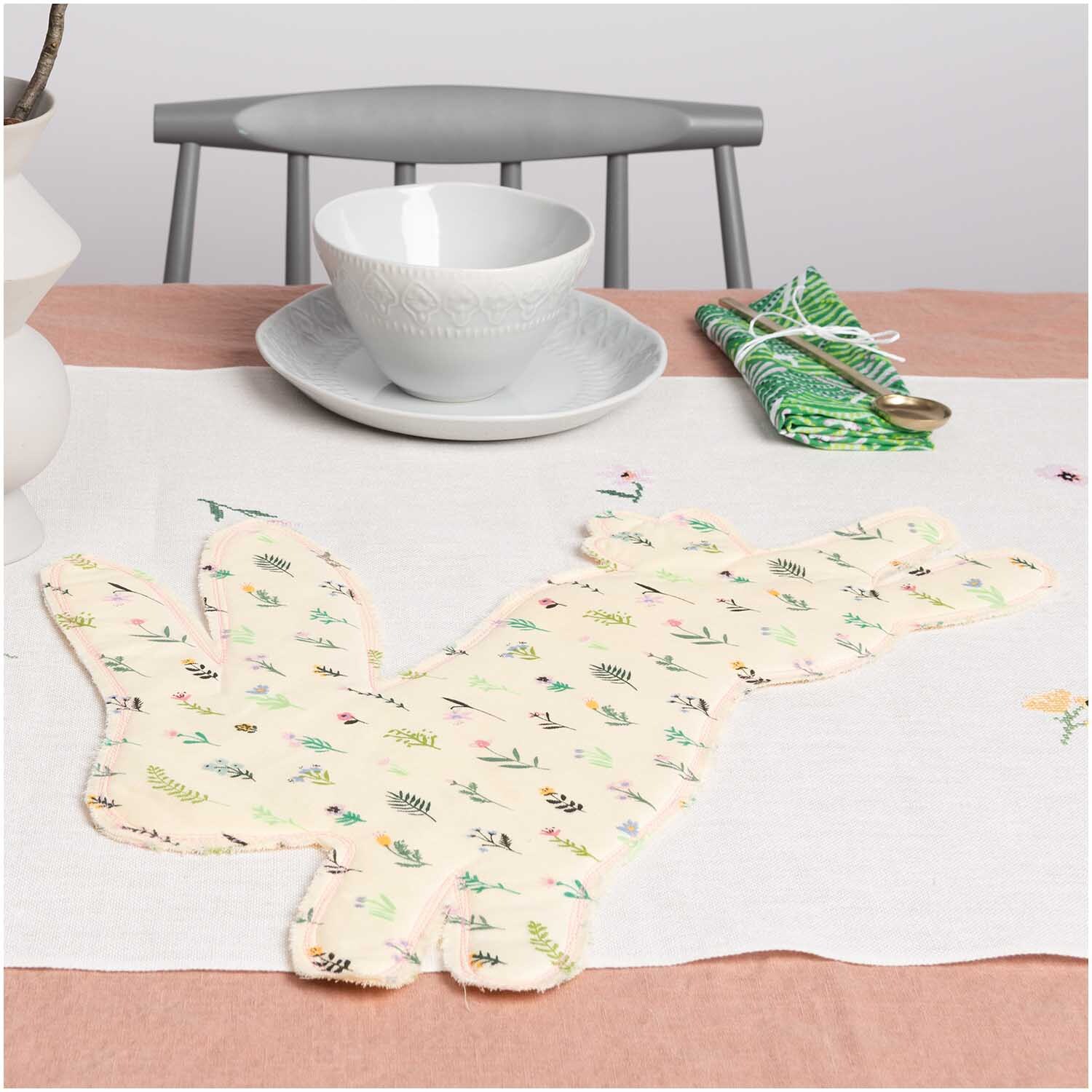 Musselin-Druckstoff Bunny Hop Streublumen auf einem Tisch mit Geschirr und Besteck, ideal für Frühlingsdekorationen.