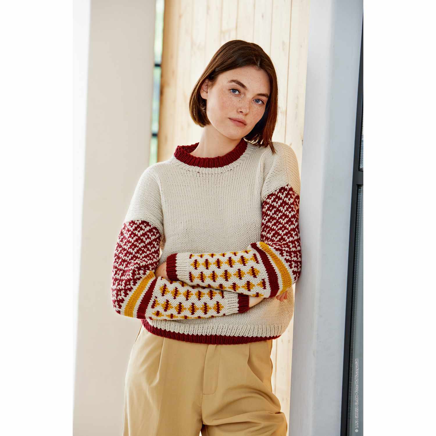 Bingo Pullover aus Lana Grossa Wolle in Creme mit roten und gelben Mustern, getragen von einer Frau.