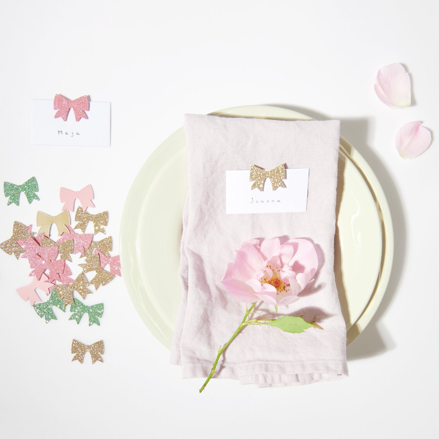 Streudekoration Schleifen Glitzer auf einem Tisch mit rosa Blume und Namenskarten, ideal für festliche Anlässe.