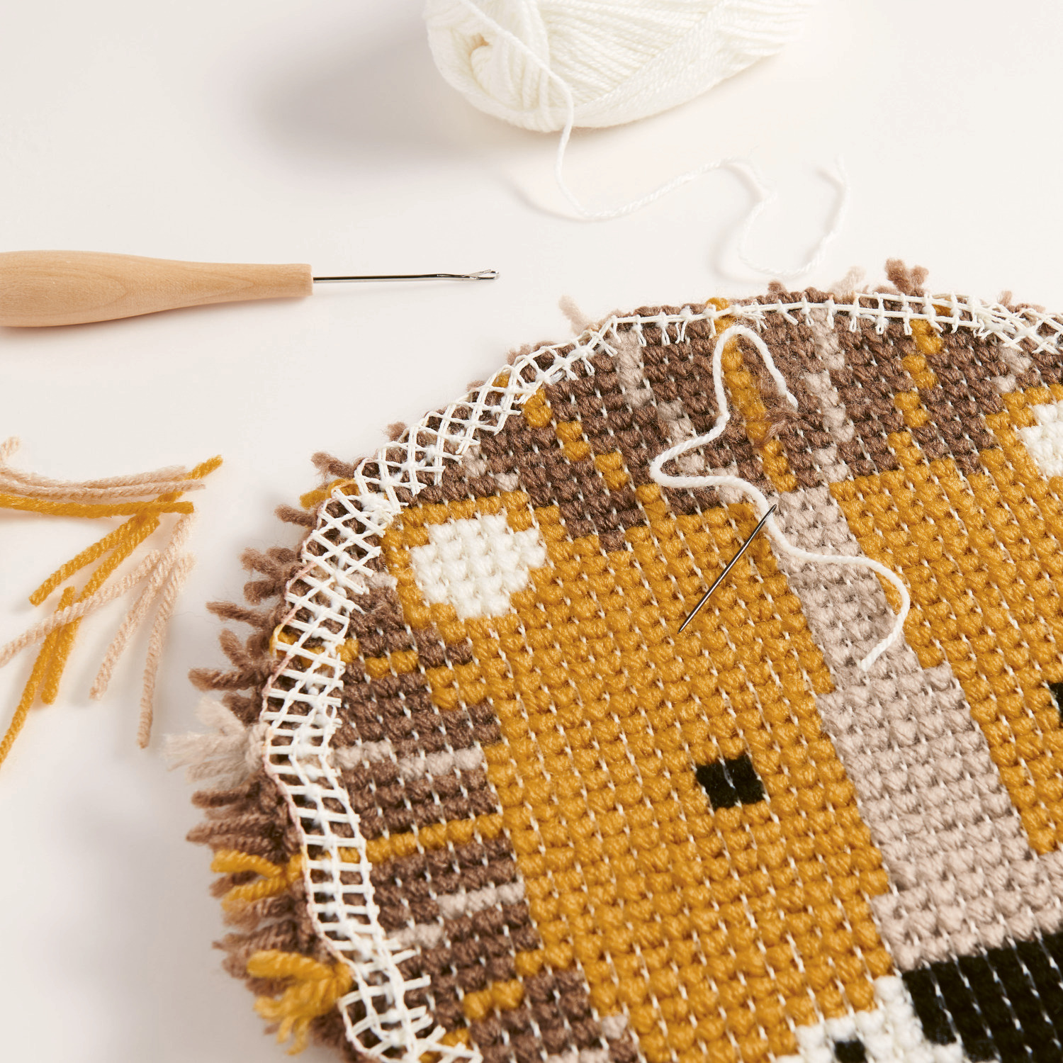 Rico Hooki Hooki Knüpfgarn zeigt ein halbfertiges Stickprojekt mit Löwenmotiv in warmen Tönen.