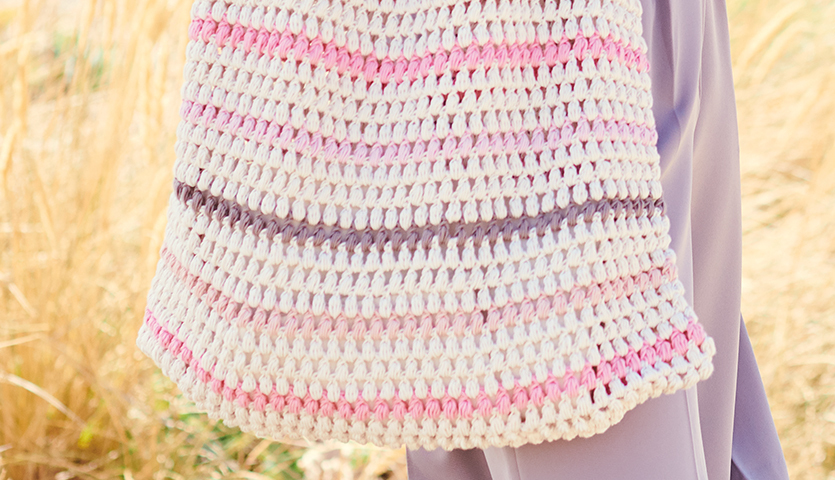 Häkelanleitung Tasche aus Essentials Organic Cotton aran, gestreift in Rosa und Weiß, getragen im Freien.