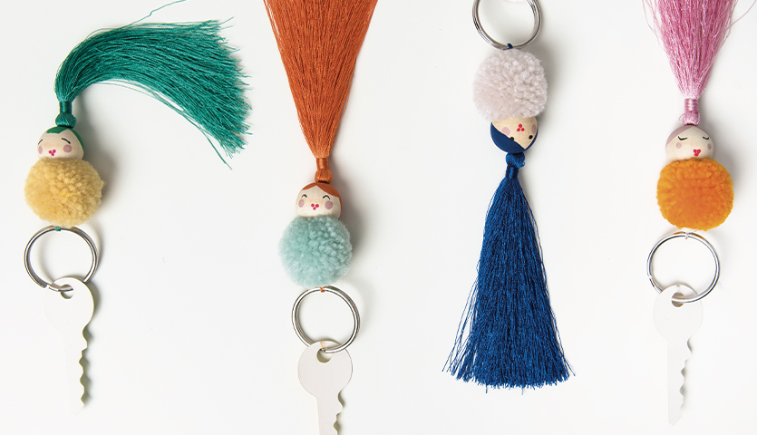 Bastelanleitung Schlüsselanhänger aus Pompons und Quasten: Vier bunte Schlüsselanhänger mit Pompons und Quasten in verschiedenen Farben.