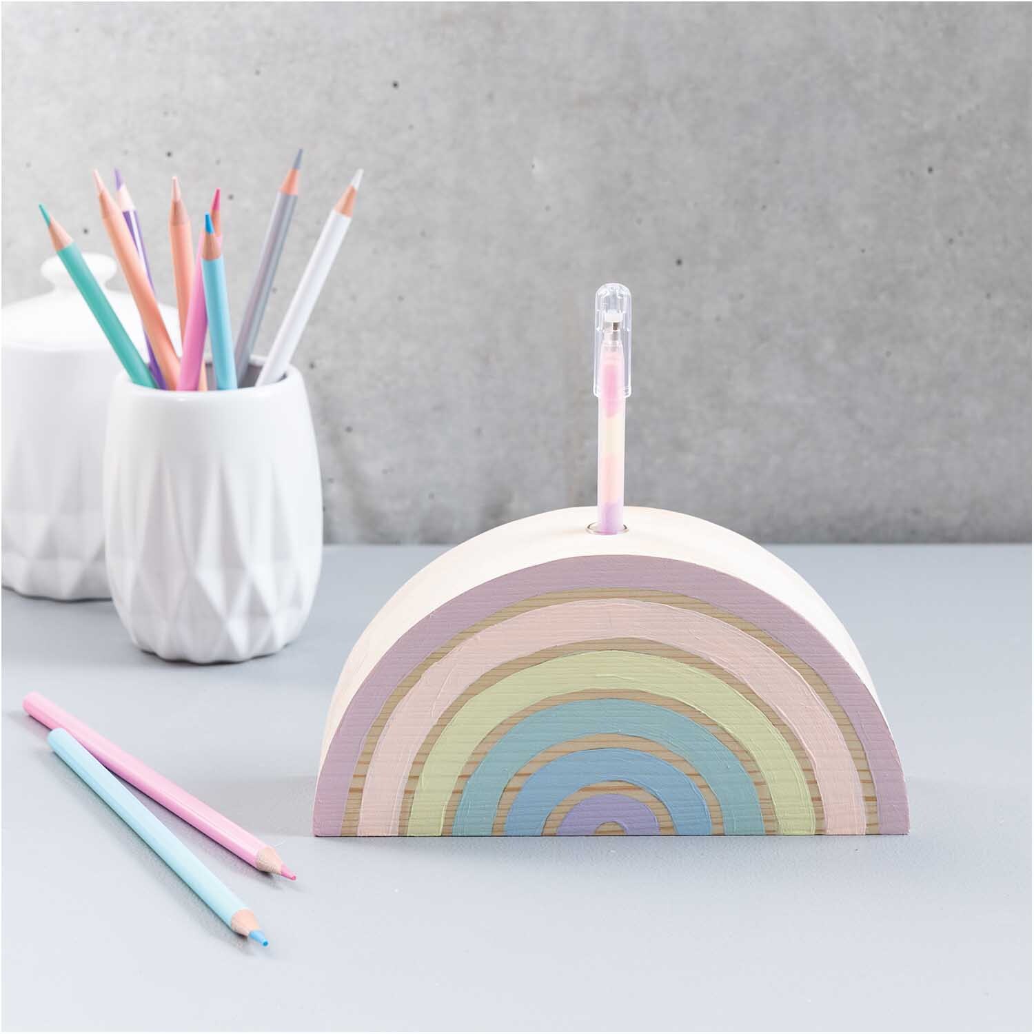 Holz-Regenbogen mit kleiner Glasvase, pastellfarben, auf einem Tisch mit Buntstiften und weißen Vasen.