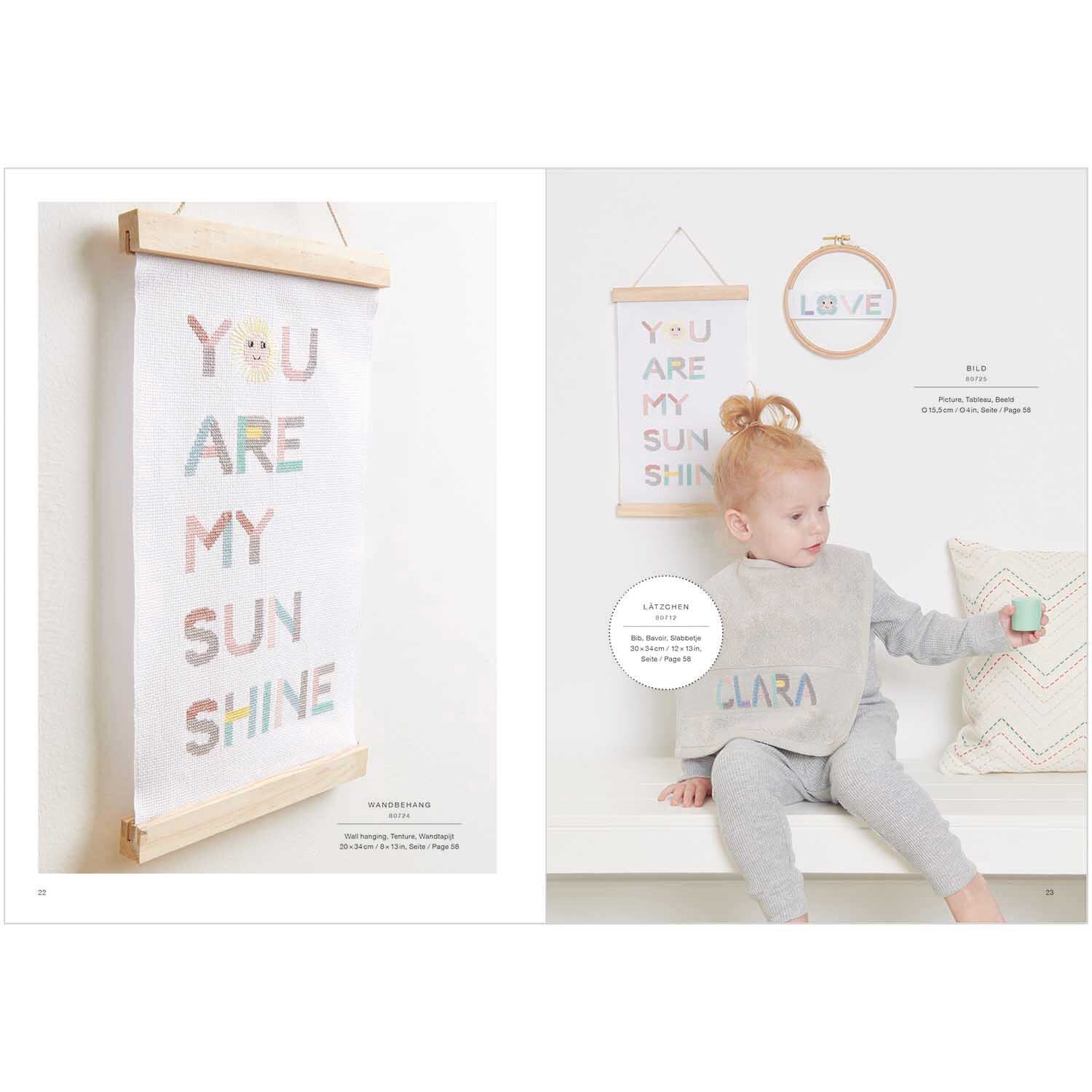 Stickbuch Happy Baby Nr. 179: Kind in grauem Outfit mit gesticktem Lätzchen, Wanddeko mit buntem Text.