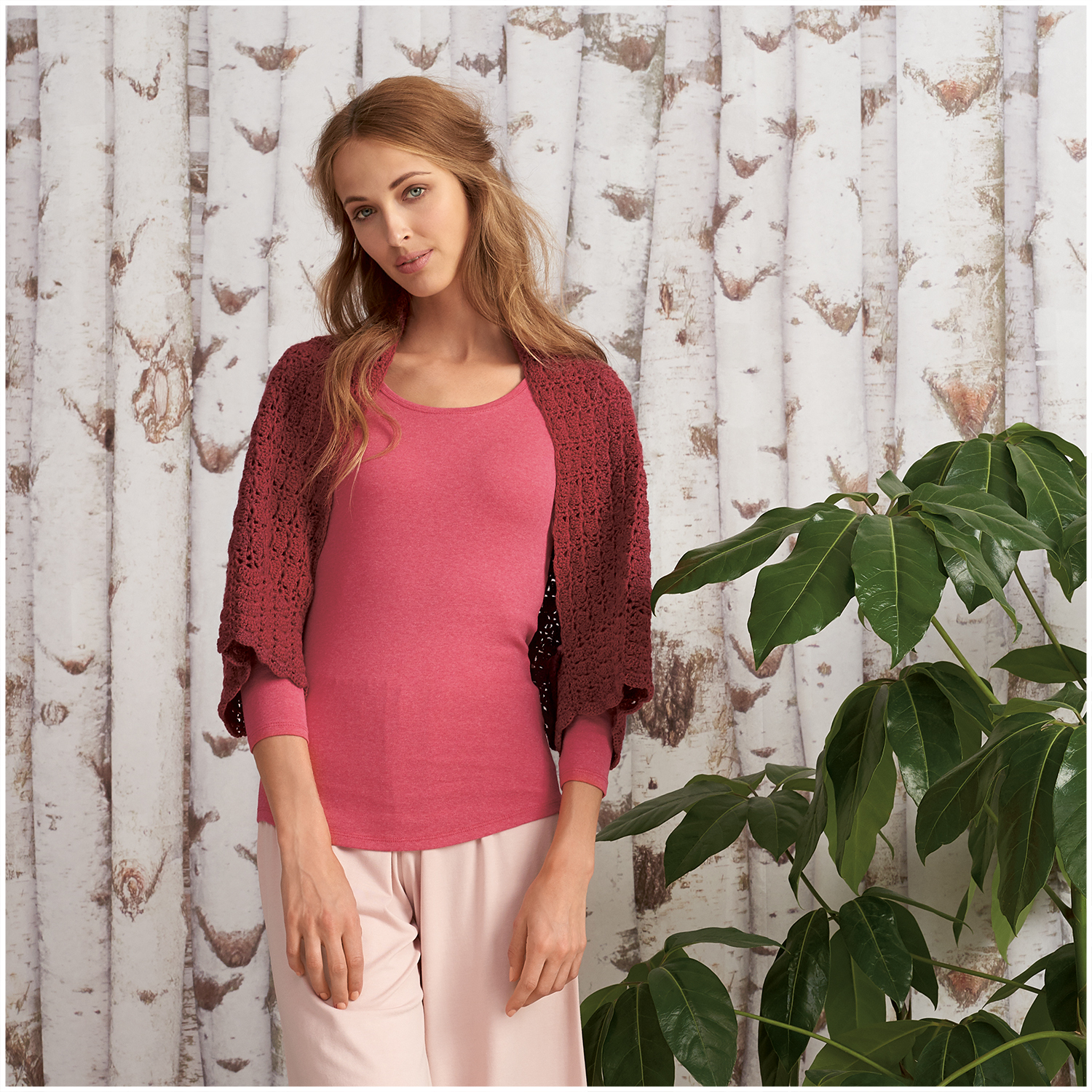 Creative Wool dégradé: Frau in rosa Pullover und Schal vor Birkenwald-Tapete, neben grüner Pflanze.