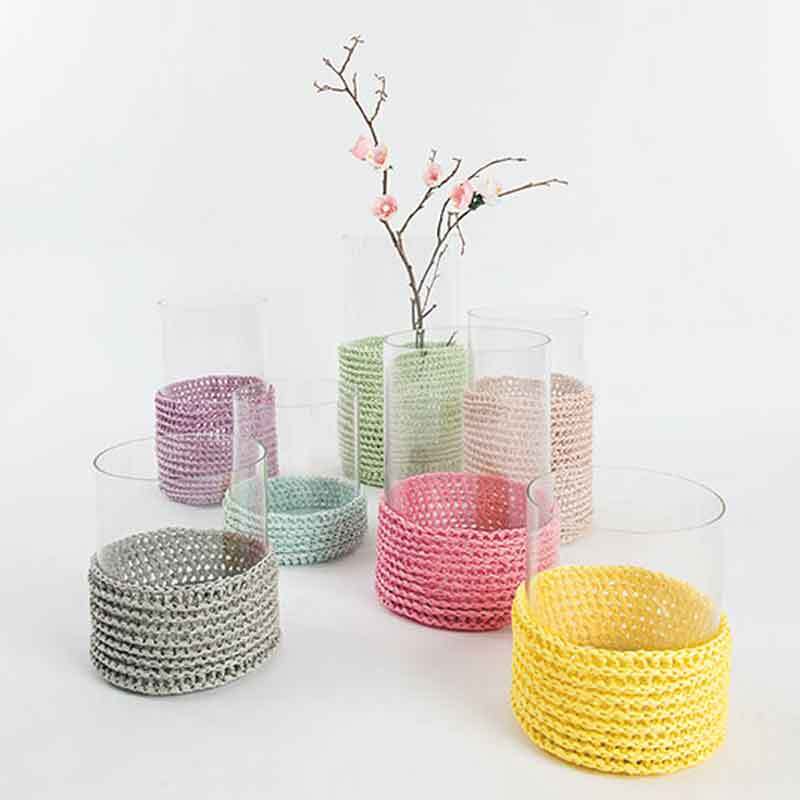 Creative Paper: Bunte, gehäkelte Überzüge aus Rico Design um Glasvasen, dekoriert mit Zweigen.