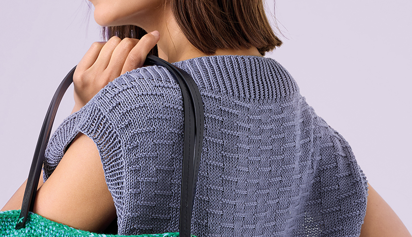 Strickanleitung Strukturmuster-Top aus Mille Fili: Frau trägt ein graues, strukturiertes Top und eine grüne Tasche über der Schulter.