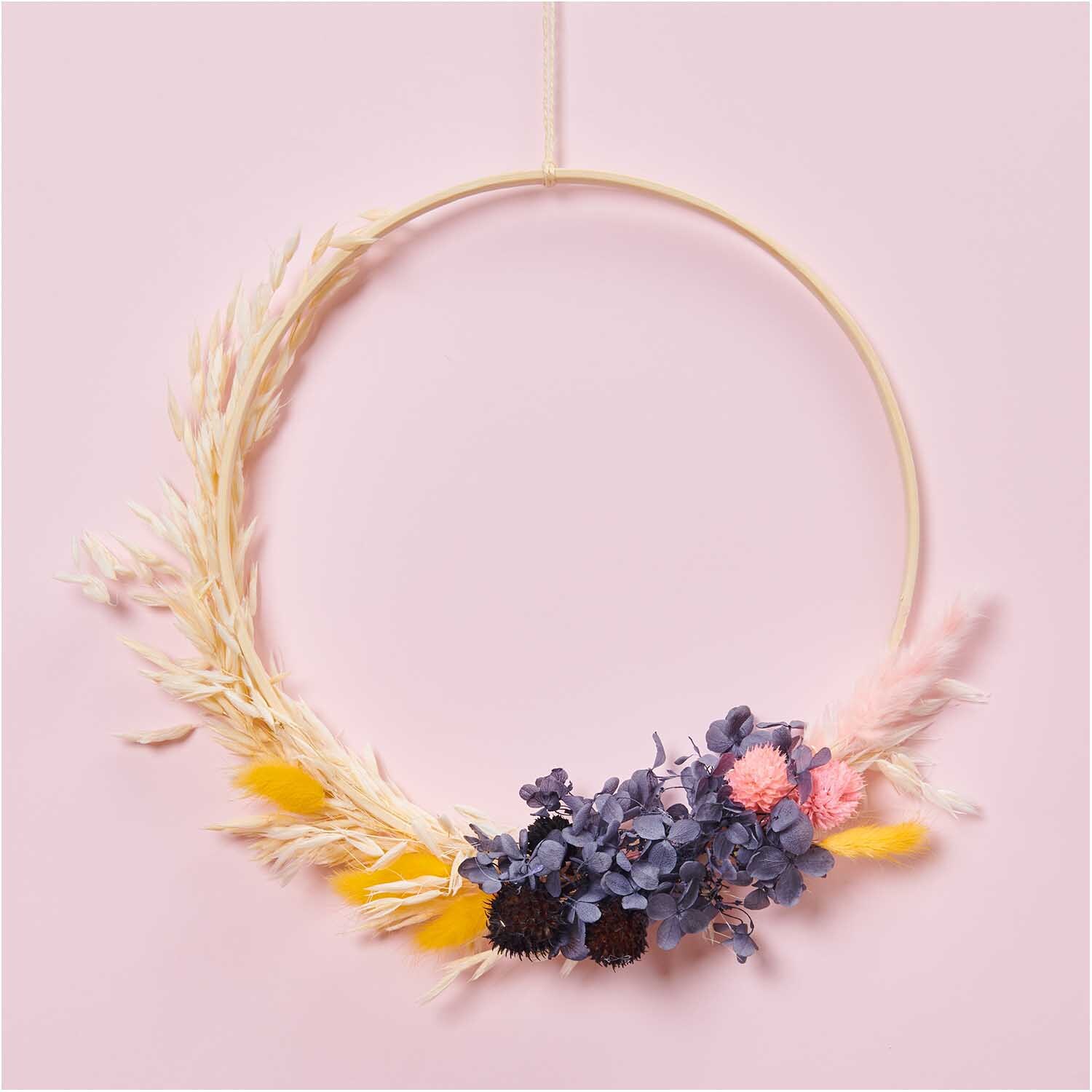Getrocknete japanische Karde schwarz 60-75cm 50g von Rico Design, dekorativ in einem Kranz mit bunten Blumen auf rosa Hintergrund arrangiert.