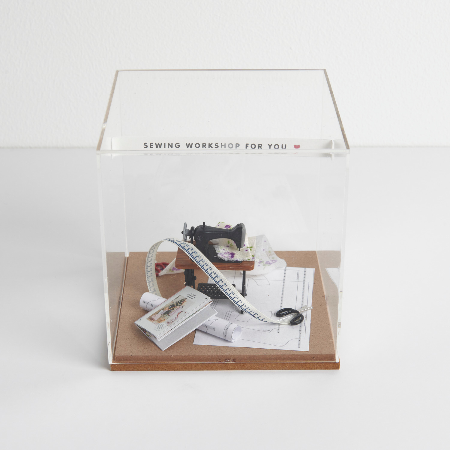 Miniatur Nähmaschine mit Stoff in einer transparenten Figurico Dekohaube, dekorativ aufgestellt.