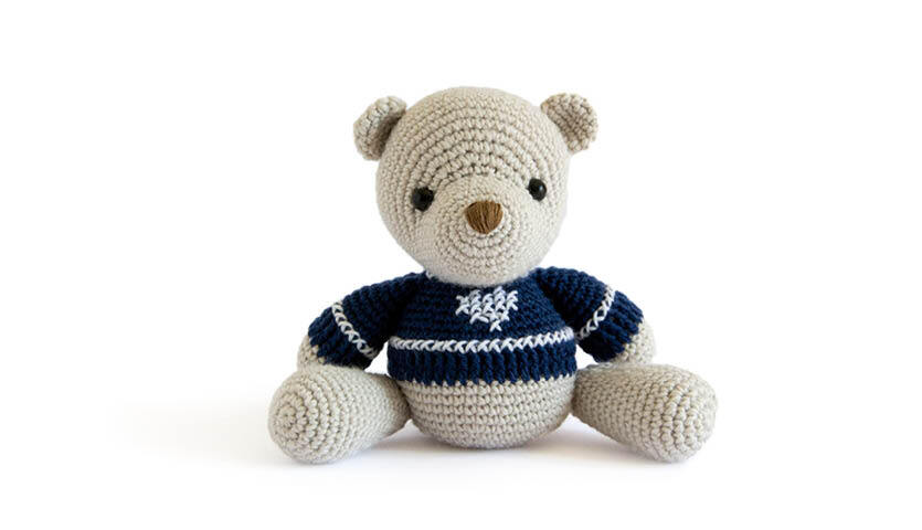 Häkelanleitung Teddybär: Ein gehäkelter Teddybär in einem blauen Pullover mit weißen Streifen sitzt aufrecht.
