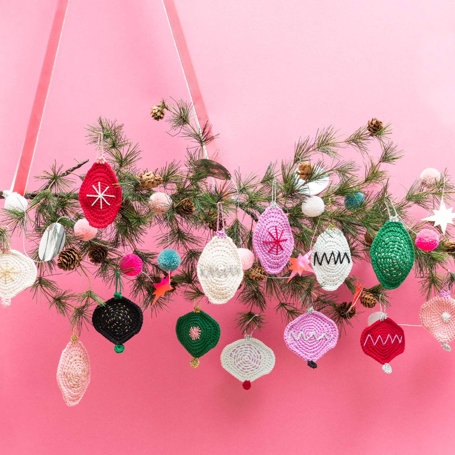 Häkelanleitung Ricorumi Christmas-Anhänger: Bunte, gehäkelte Weihnachtsanhänger an einem Tannenzweig vor rosa Hintergrund.