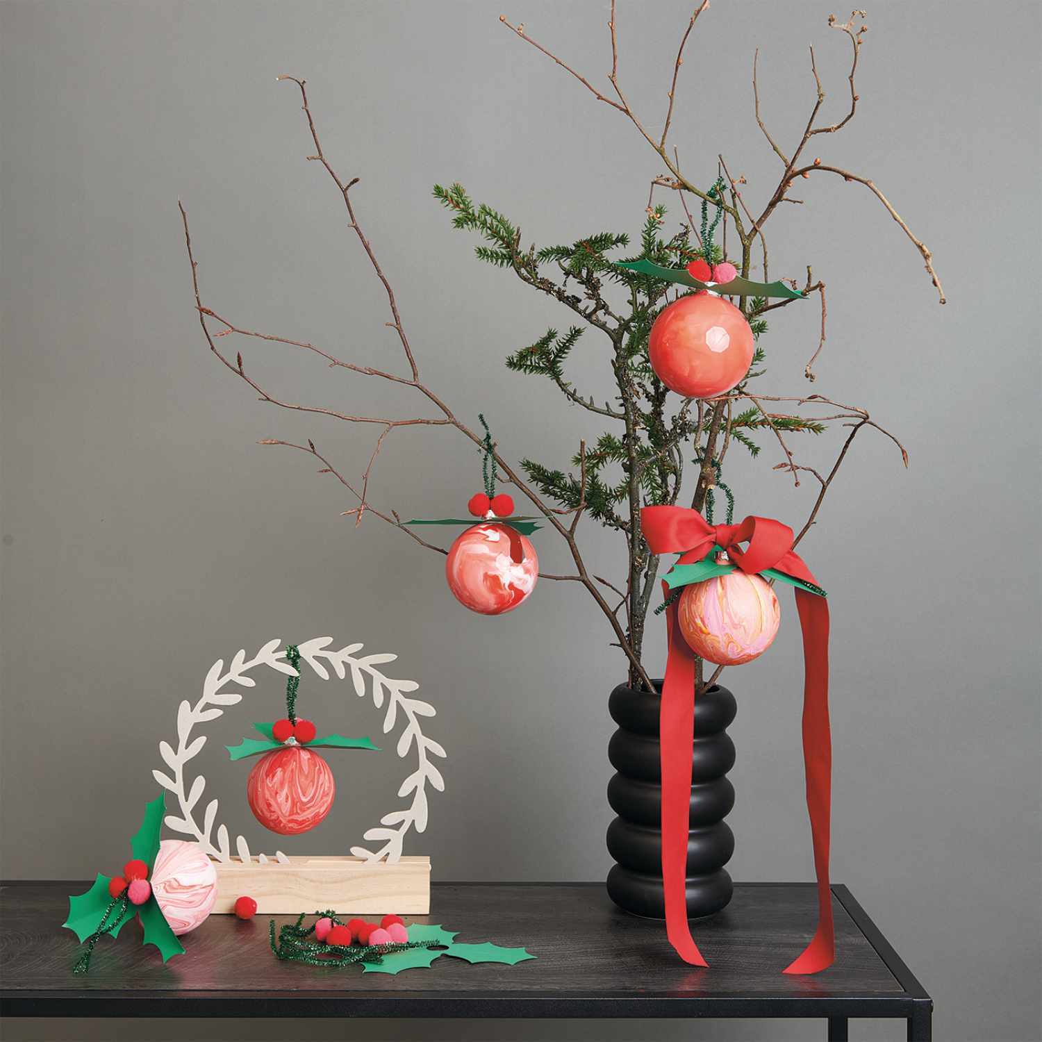 Anleitung Christbaumkugeln mit Pouring gestalten: Rote Kugeln an einem kahlen Ast in schwarzer Vase, dekoriert mit Schleifen.