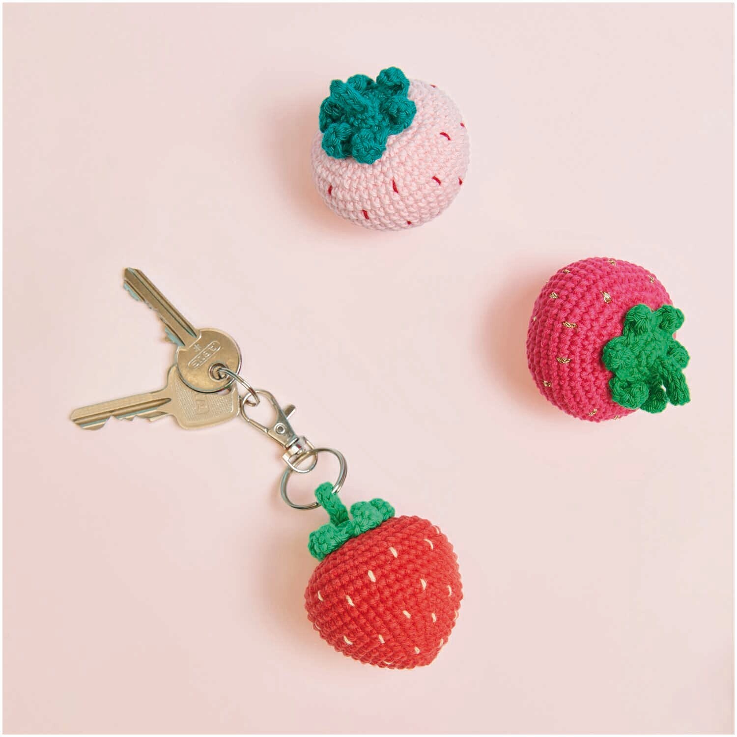 Creative Ricorumi dk: Drei gehäkelte Erdbeeren, eine als Schlüsselanhänger, auf rosa Hintergrund.