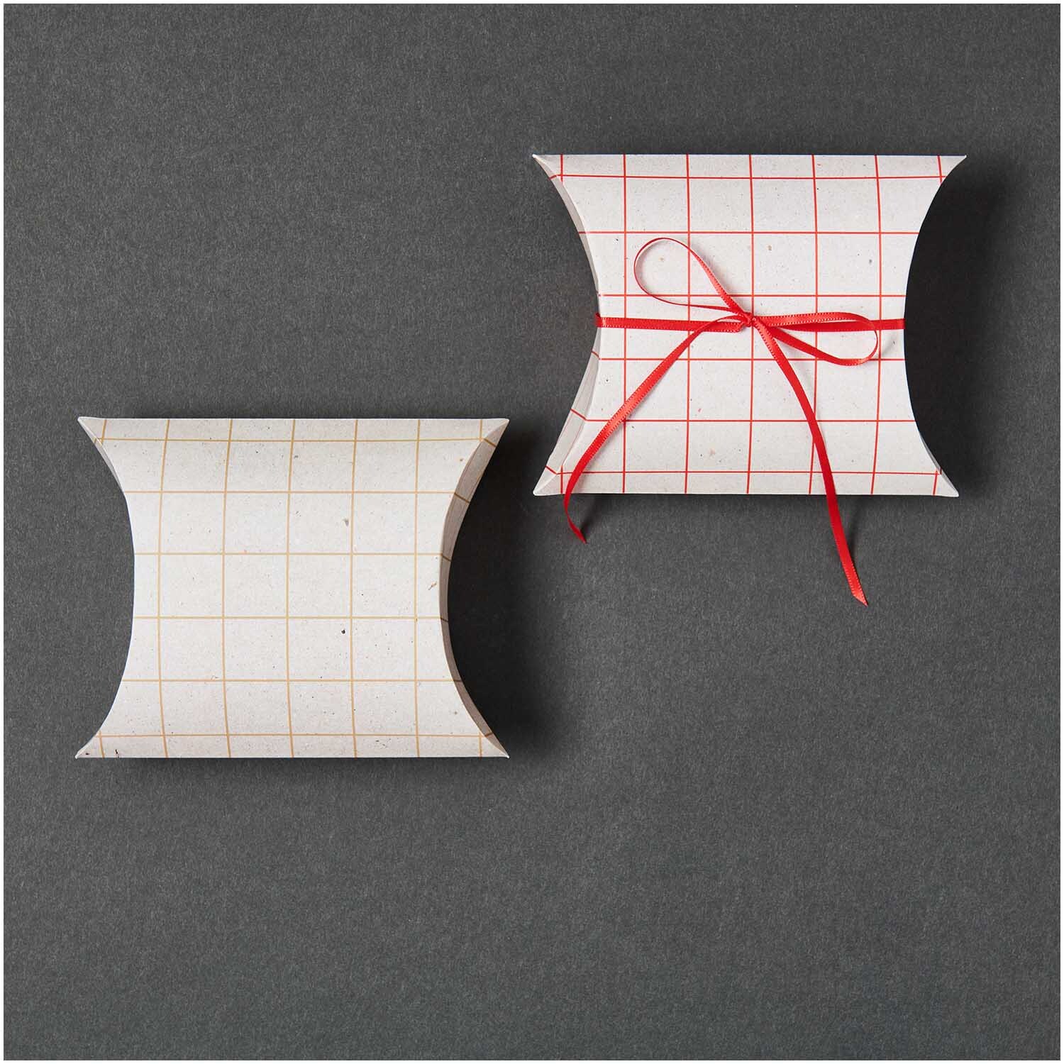 Paper Poetry Geschenkschachteln aus Graukarton mit kariertem Muster, eine mit rotem Band verziert.