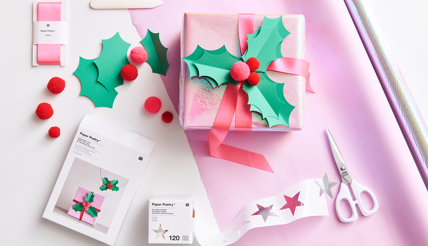 Bastelanleitung Ilex-Geschenkverzierung: Geschenk mit grünen Ilex-Blättern und roten Beeren dekoriert, umgeben von Bastelmaterialien auf rosa Untergrund.