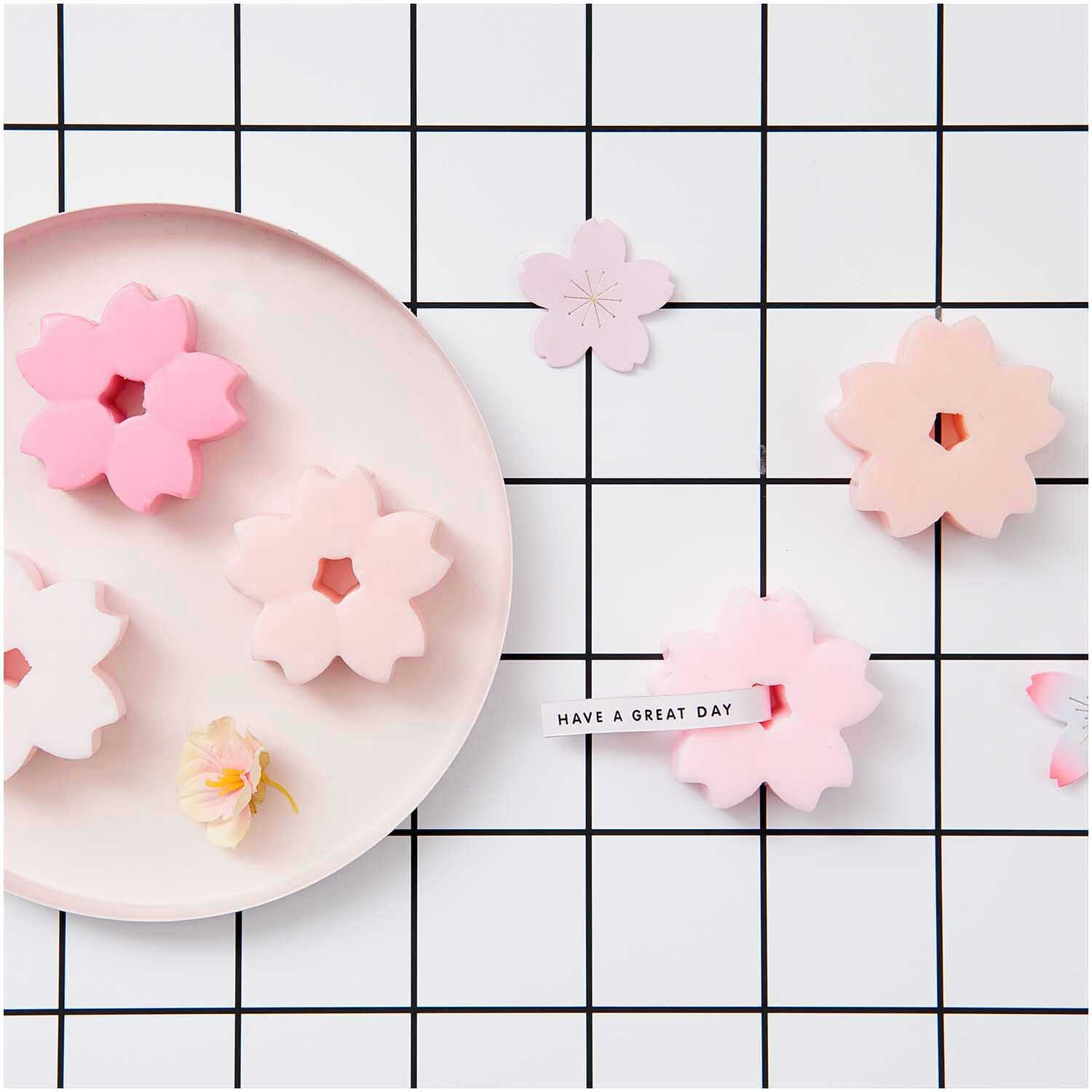 Seifengießform Kirschblüten von Rico Design auf einem Gitterhintergrund mit rosa Blütenformen.