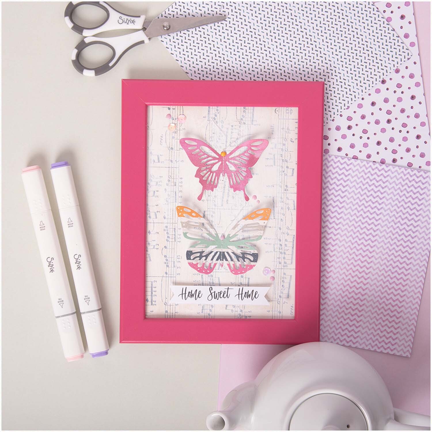 Thinlits Die Set Butterflies in einem pinken Rahmen mit Schmetterlingsdesign und "Home Sweet Home"-Text, umgeben von Bastelmaterialien.