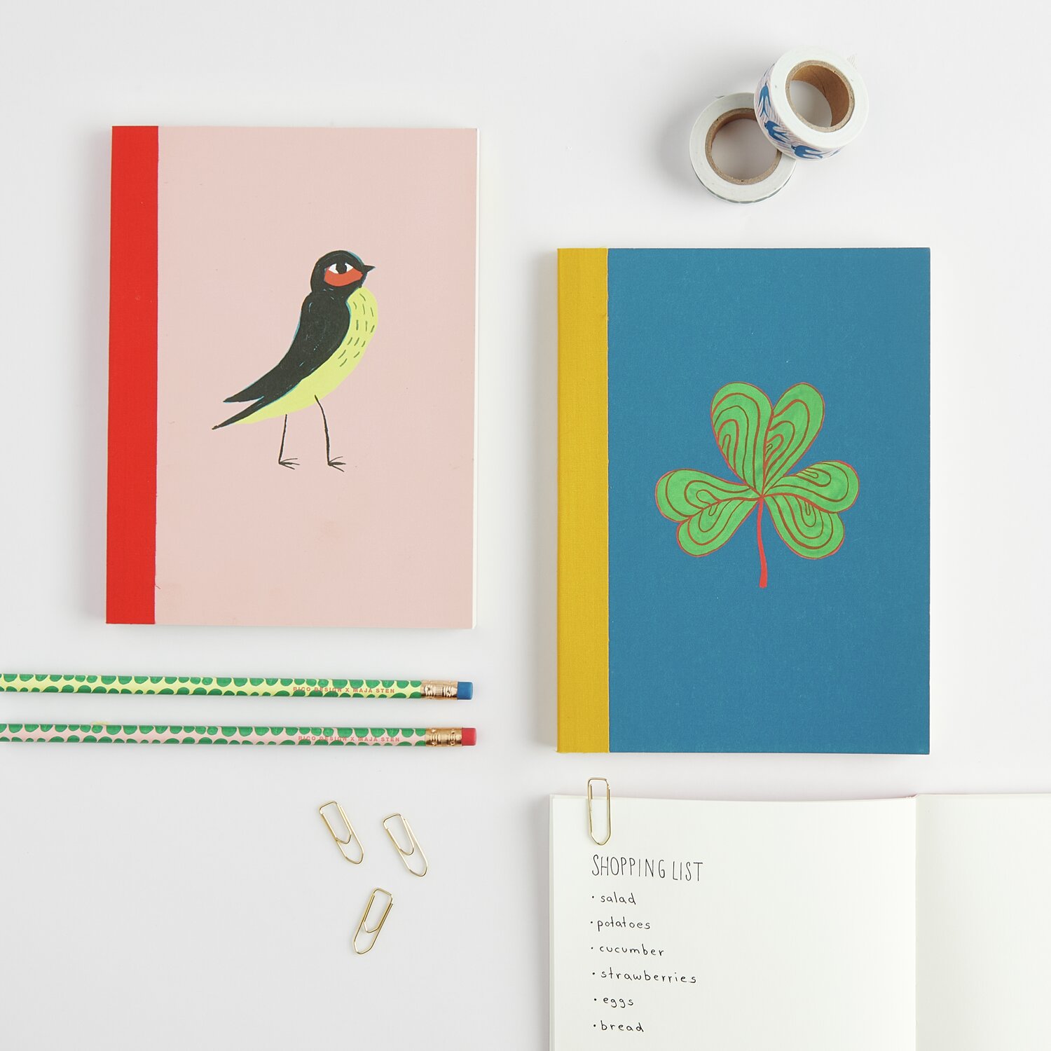 Notizbuch Midsommar Magic Kleeblatt und Vogel von Rico Design in Rosa und Blau mit bunten Covern, abgebildet mit Stiften und Büroklammern.
