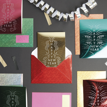 Verschiedene Karten und Umschläge mit „HAPPY NEW YEAR“ Schriftzug. Flatlay von Produkten.