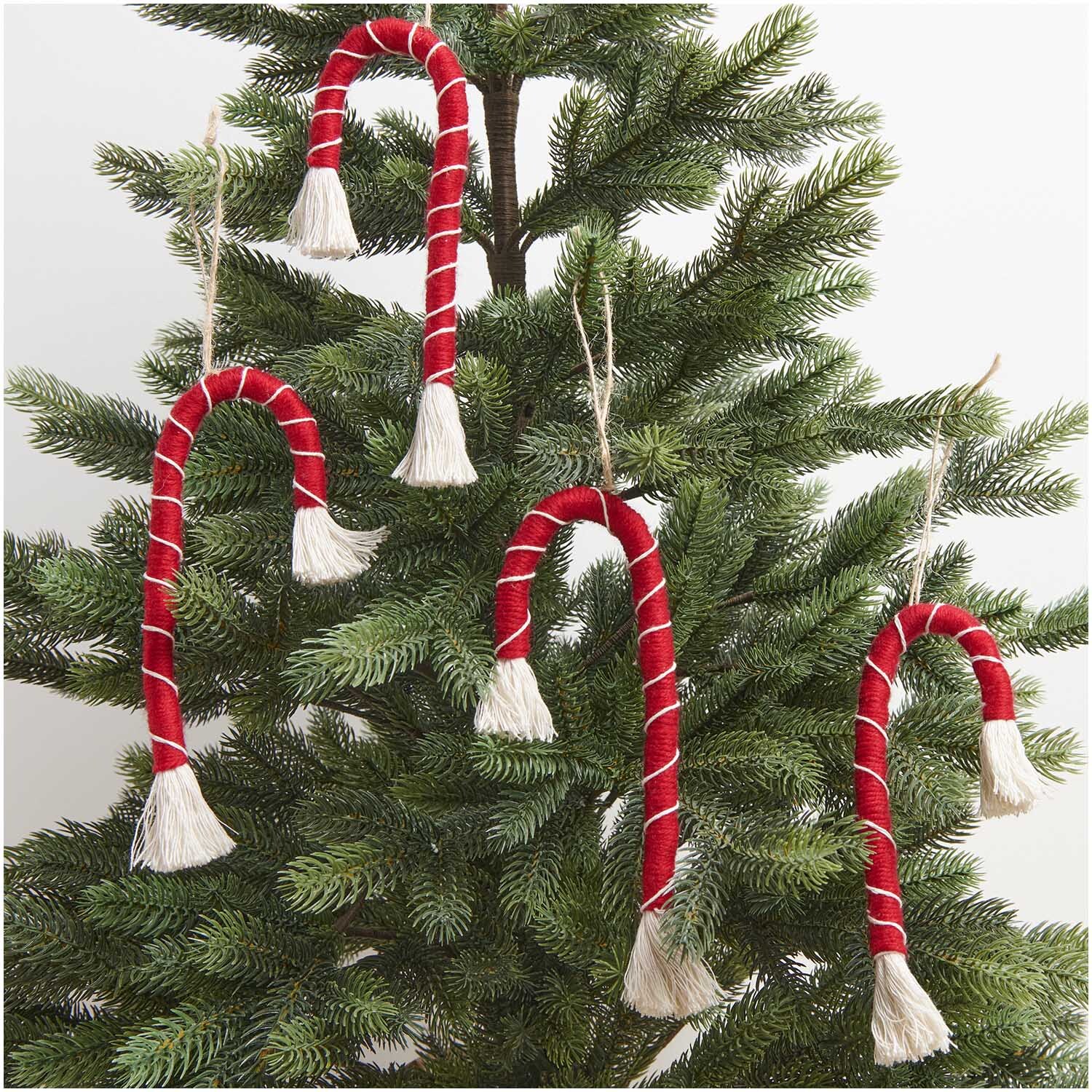 Makramee Set Zuckerstange von Rico Design: Vier rote Zuckerstangen aus Makramee hängen an einem Tannenbaum.