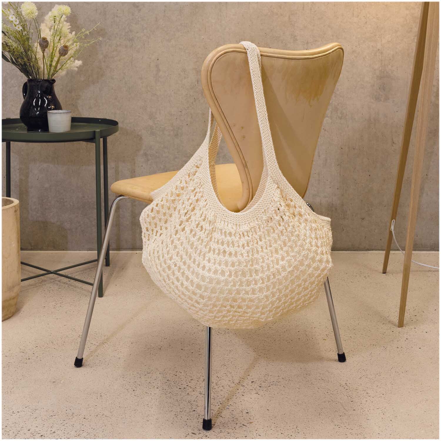 Creative Cotton aran: Handgefertigte Tasche aus Naturfasern auf einem Stuhl, umgeben von minimalistischer Einrichtung.