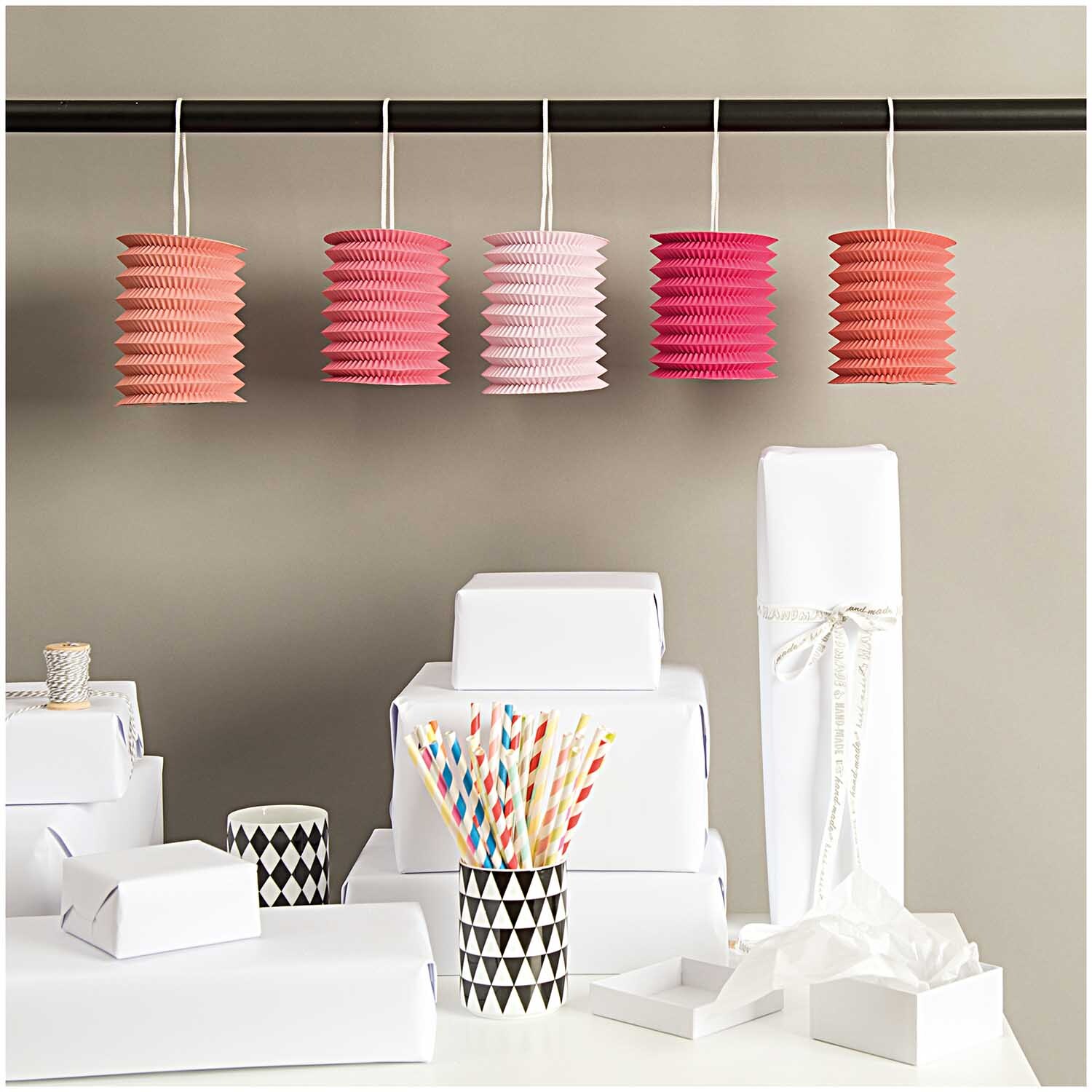 Zuglaterne candy 10x13cm Papier 5 Stück in verschiedenen Pinktönen von Rico Design, dekorativ aufgehängt über einem Tisch mit Geschenkboxen und Partyzubehör.