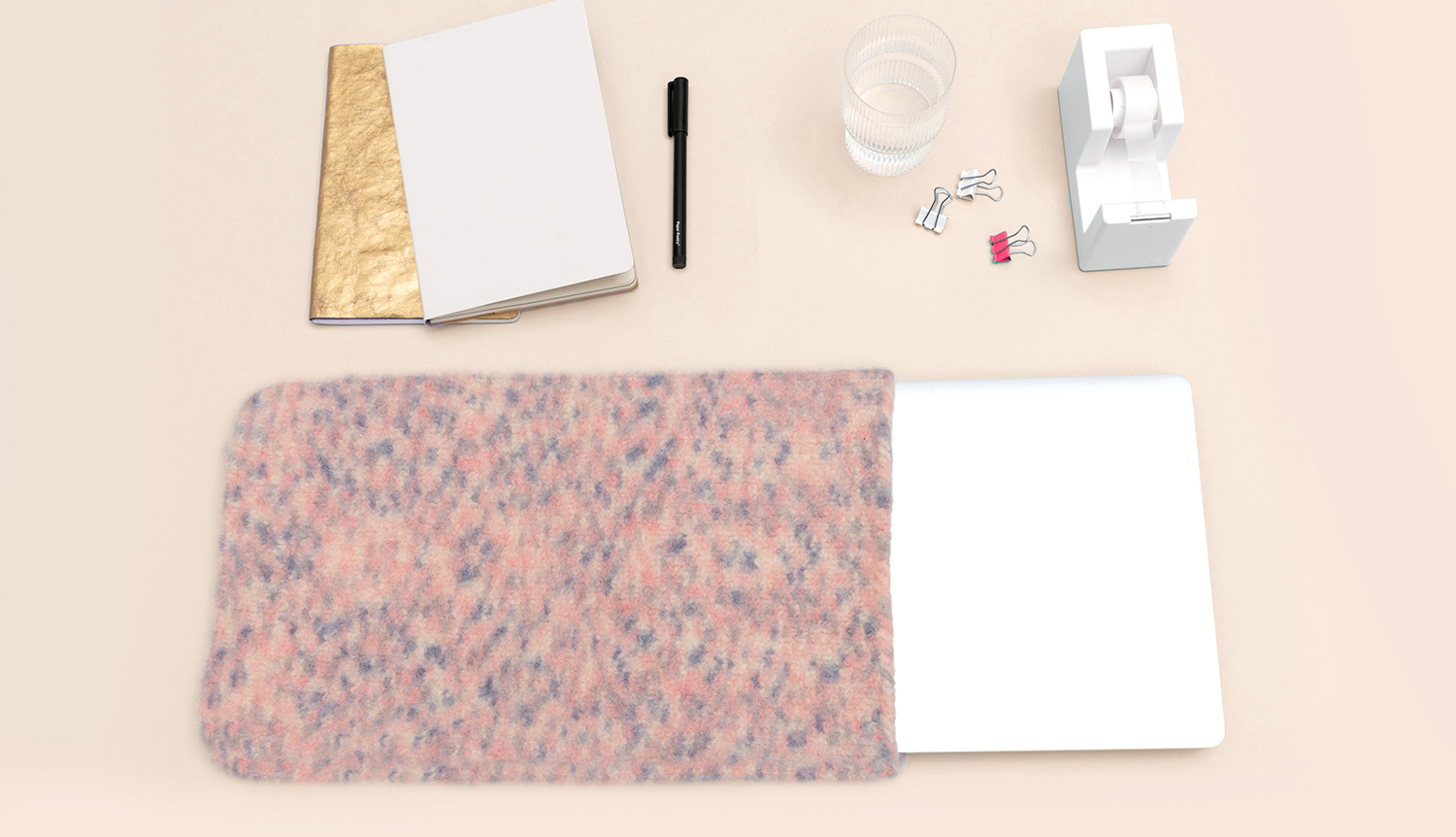 Strick-/Häkelanleitung Filz-Laptoptasche: Eine rosa-graue Filztasche mit Laptop, umgeben von Büroartikeln auf einem Tisch.