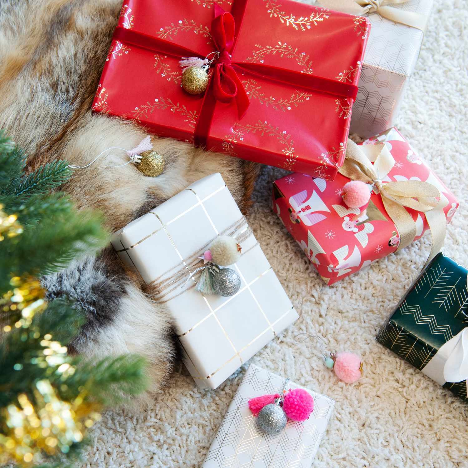 Pompon- und Kugel-Anhänger neon-pastell 6 Stück dekorieren festlich verpackte Geschenke auf einem Teppich neben einem Weihnachtsbaum.