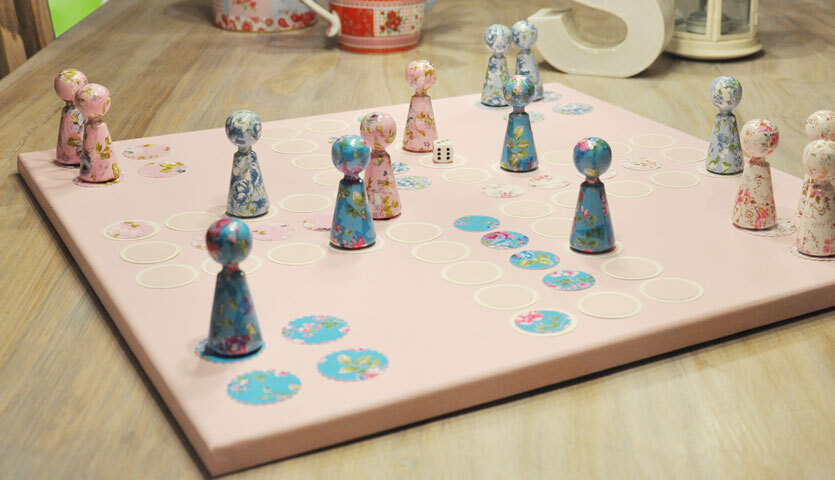 Bastelanleitung Brettspiel: Ein handgefertigtes Brettspiel mit bemalten Spielfiguren auf einem rosa Spielbrett.
