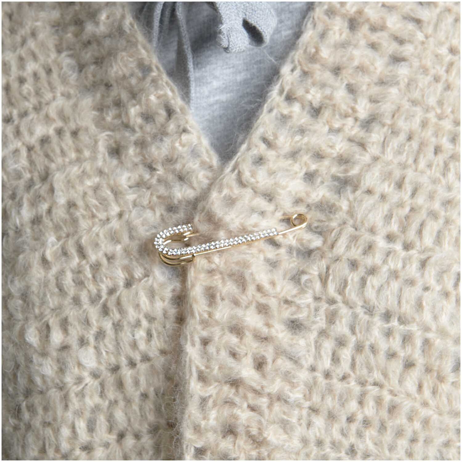 Kiltnadel mit Strass von Rico Design, befestigt an einem beigen Strickstoff, 7 cm lang.