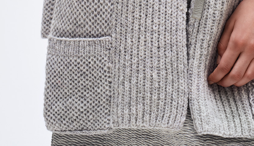 Strickanleitung Jacke aus Fashion Alpaca Dream dk: Detailaufnahme einer grauen Strickjacke mit Taschen und feiner Textur.