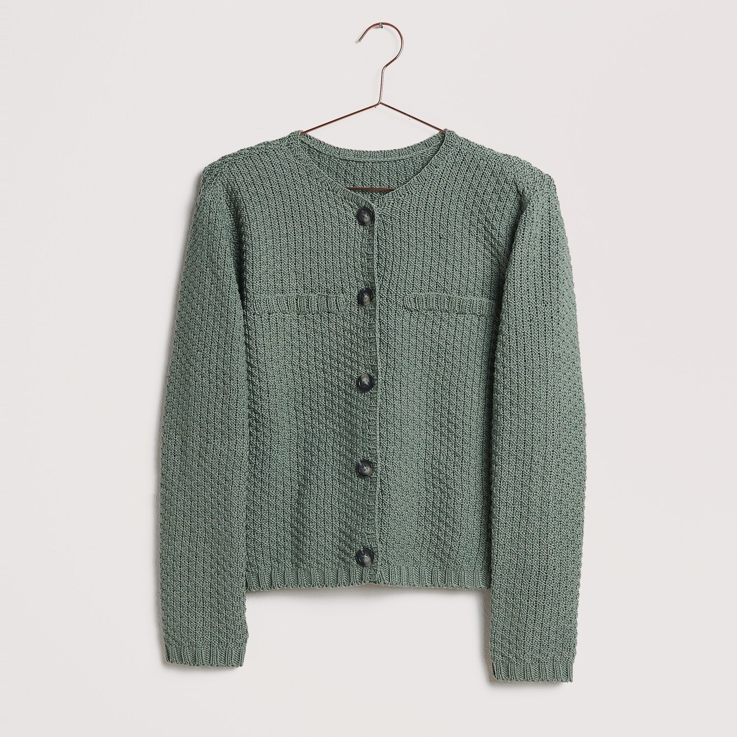 Strickset Jacke Modell 18 aus Die Neue Masche No. 12, in Salbei, auf einem Kleiderbügel präsentiert.