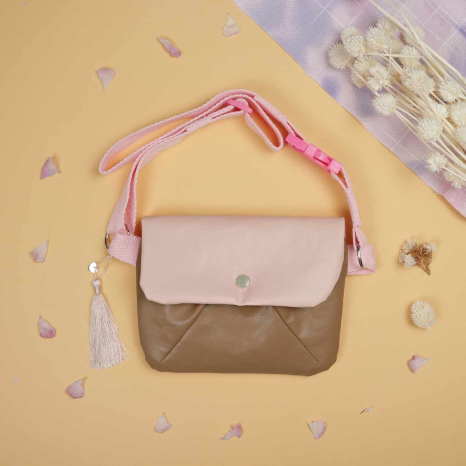 Nähanleitung Bauchtasche: Stilvolle Bauchtasche in Rosa und Braun auf beigem Hintergrund mit Blüten.