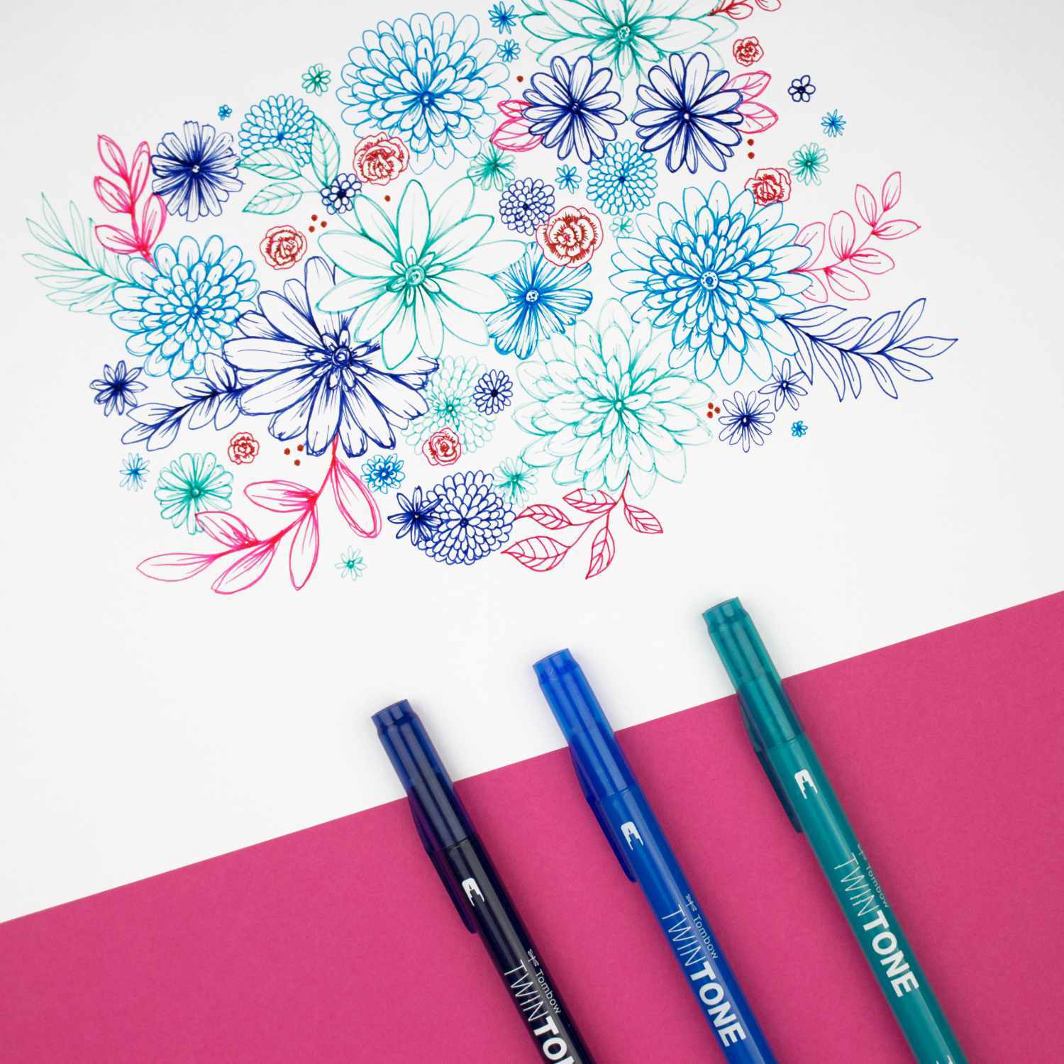 TwinTone Fasermaler zeichnen bunte Blumen auf weißem Papier. Drei Stifte in Blau, Türkis und Pink liegen auf rosa Untergrund.