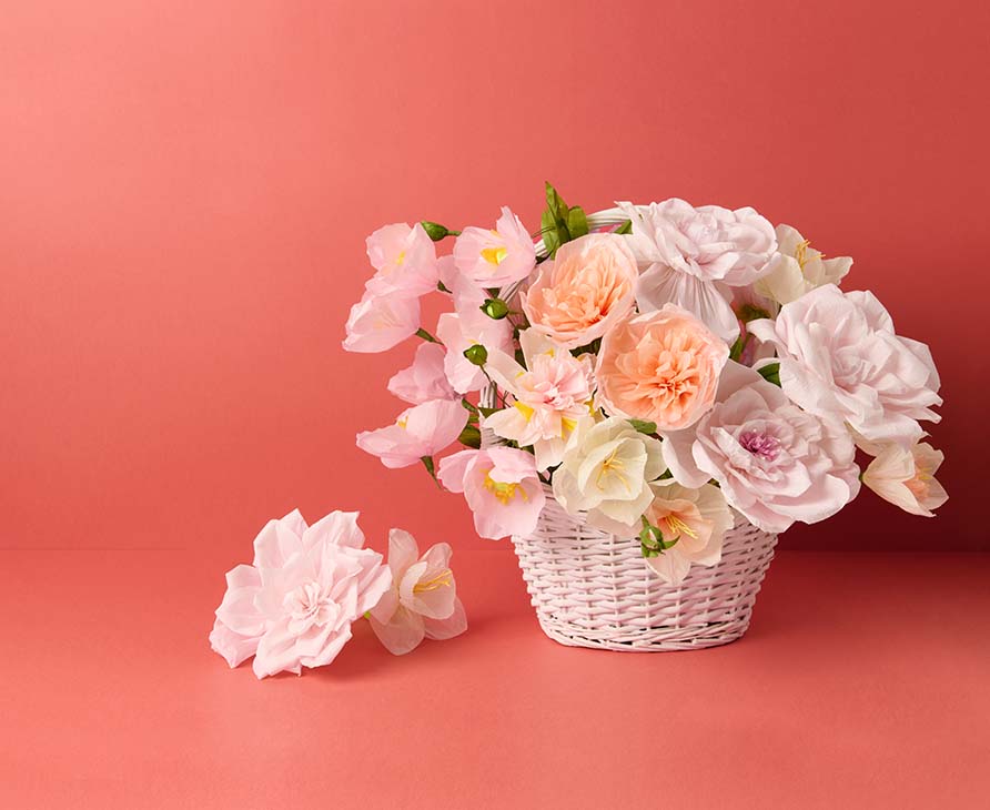 Verschiedenen rosa farbige Papierblumen in einem weiß geflochtenen Korb. Produkte aus der Kollektion La Vie en Rose.