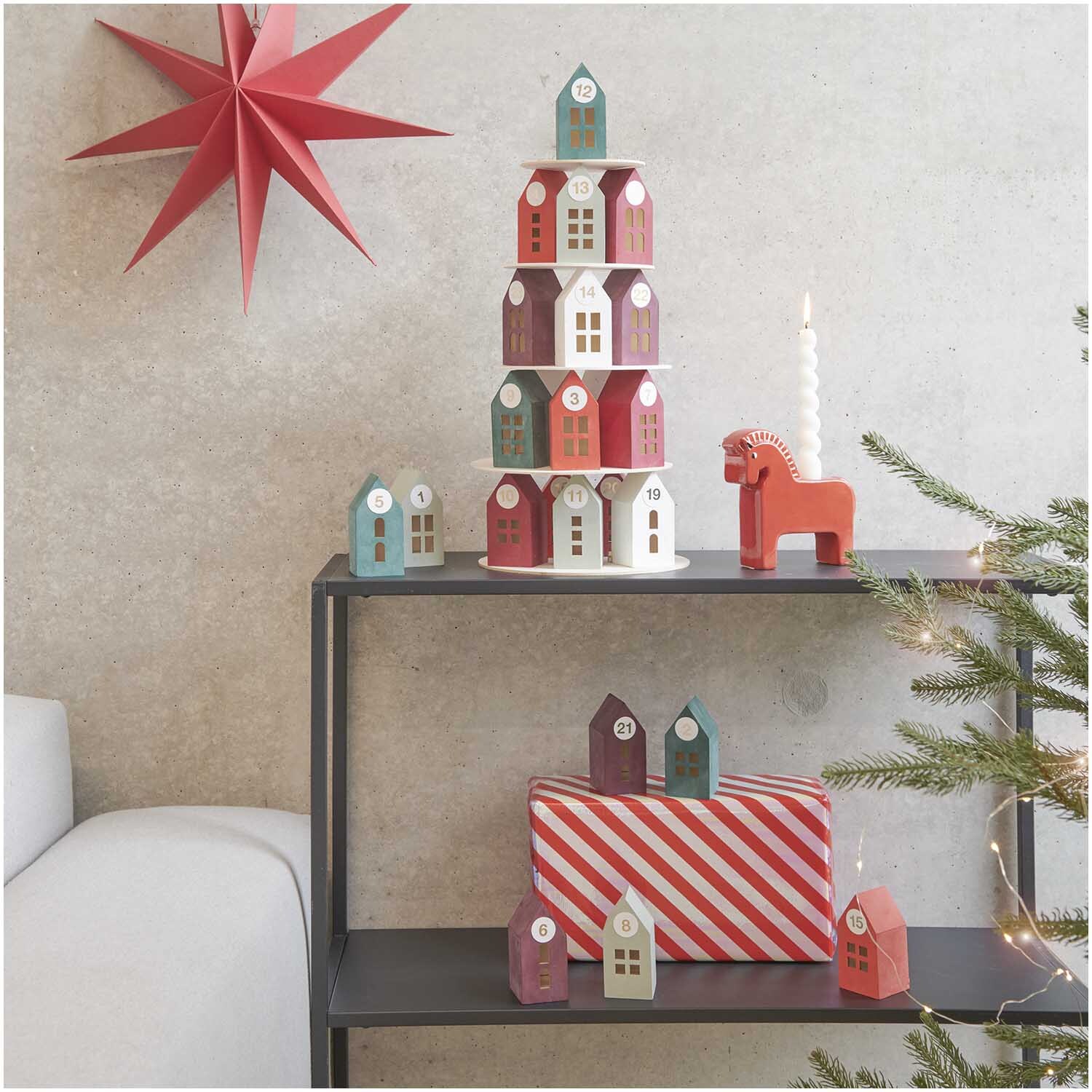 Adventskalender Holz-Haus-Pyramide von Rico Design auf Regal mit rotem Stern und Geschenk.