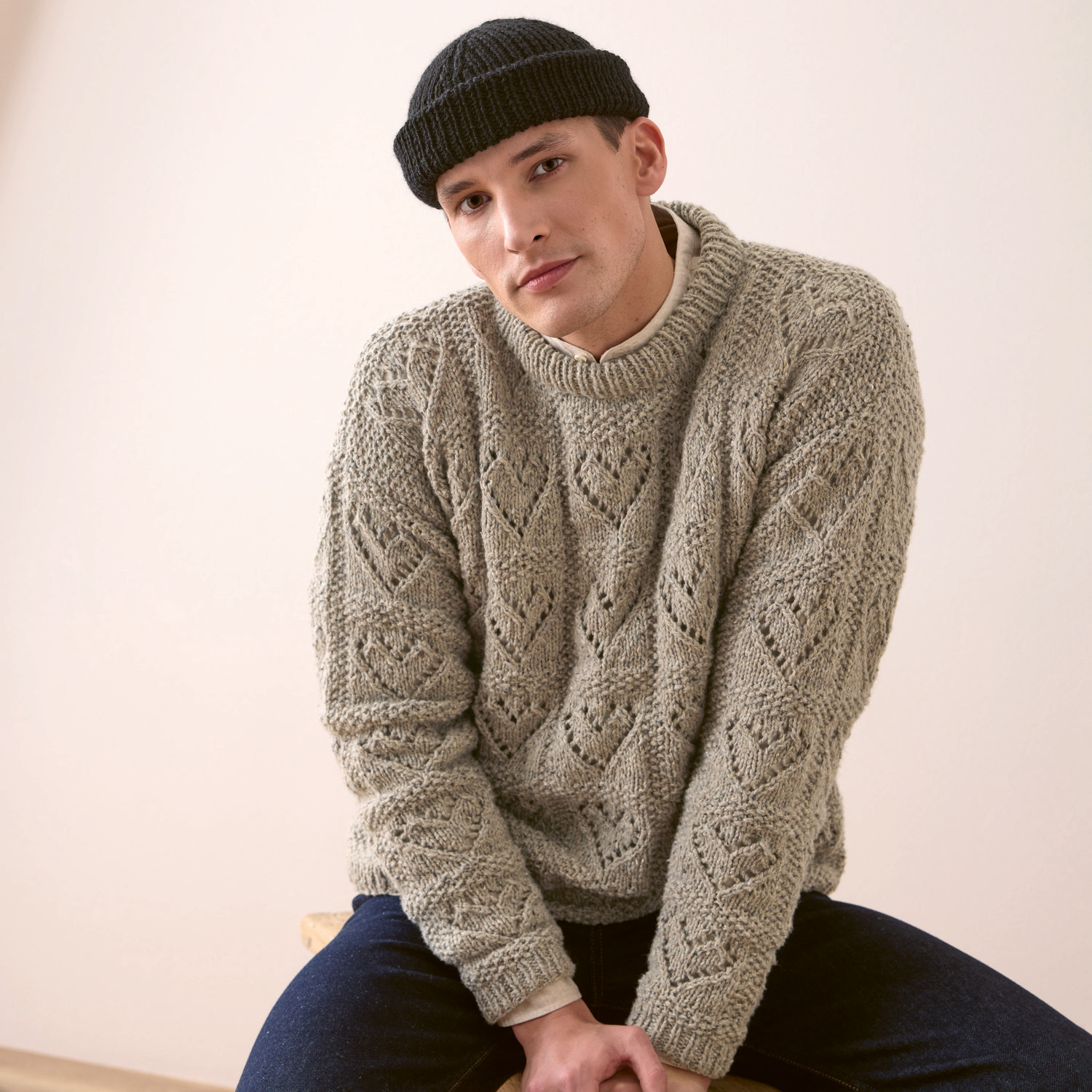 Strickset Herrenpullover Modell 06: Mann trägt grauen Strickpullover mit Zopfmuster und schwarze Mütze.