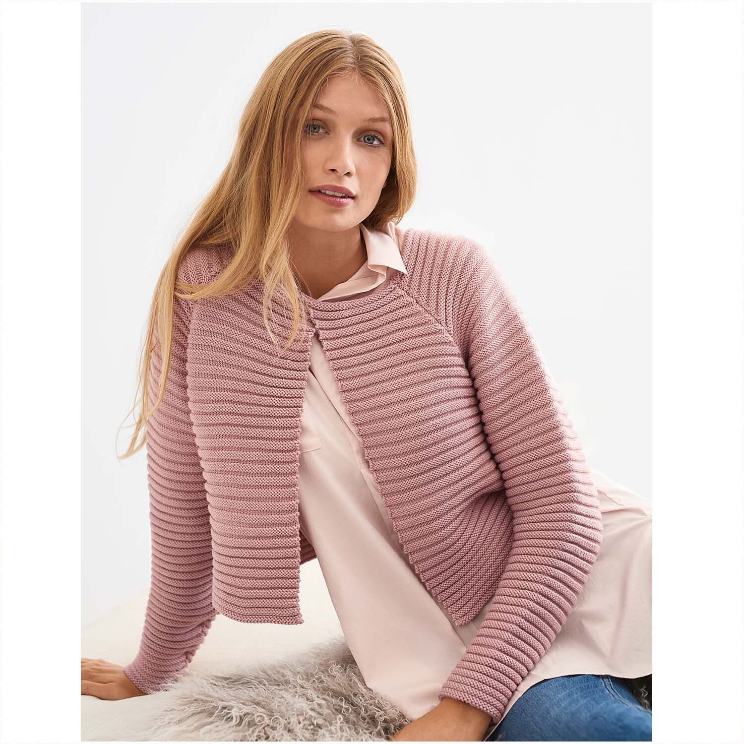 Siena Strickjacke aus Wolle Rödel in zartem Rosa, getragen von einer Frau auf einem Stuhl sitzend.