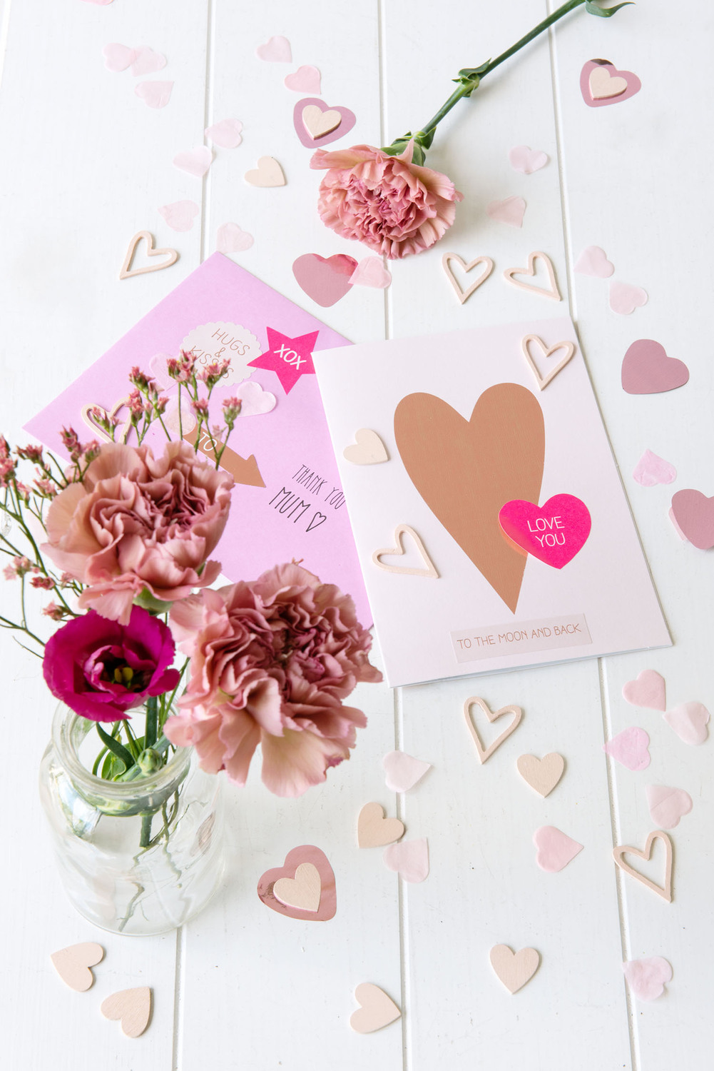 Paper Poetry Grußkartenset mit Herzmotiv und Blumen auf weißem Tisch, umgeben von rosa Herzen.