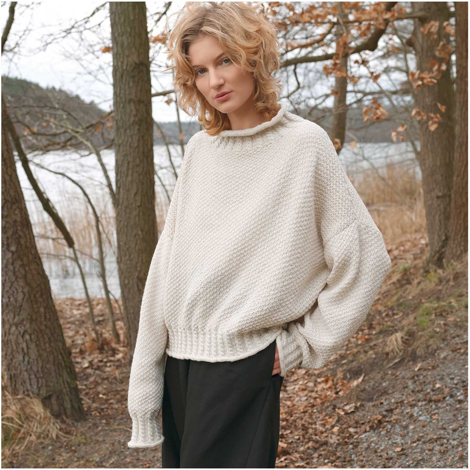 Essentials Fine Fine Merino Pullover in Creme von Rico Design, getragen von einer Person in herbstlicher Waldlandschaft.