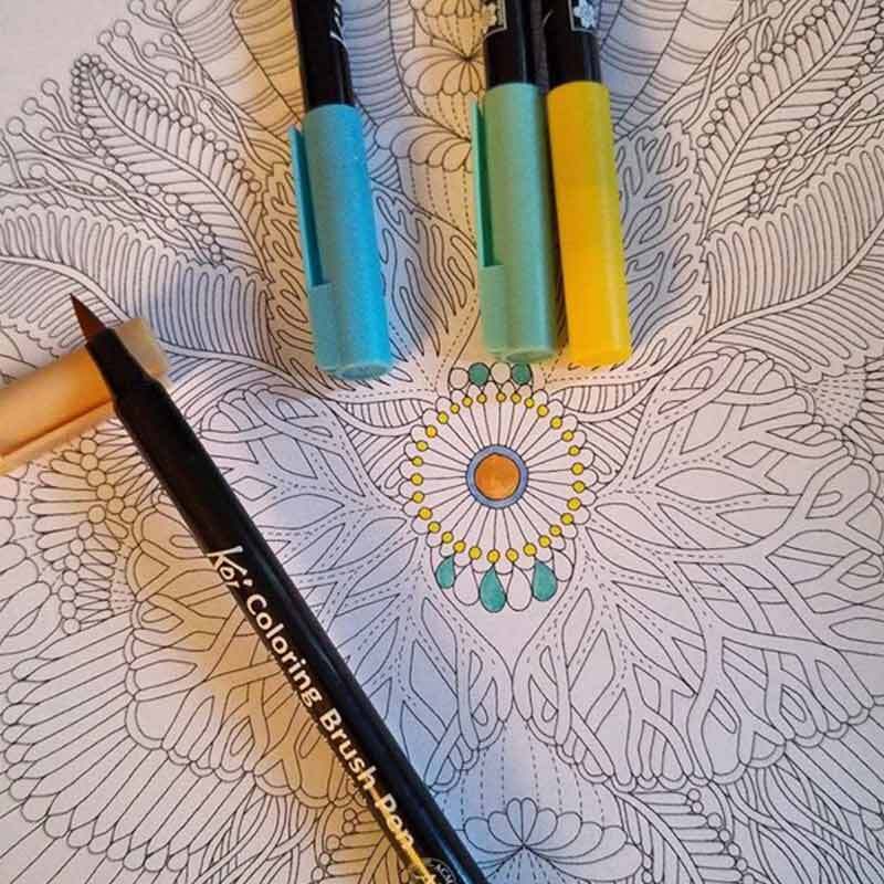 Coloring Brush Pen: Drei Koi-Stifte in Blau, Grün und Gelb auf einem detaillierten Mandala-Malbuch.