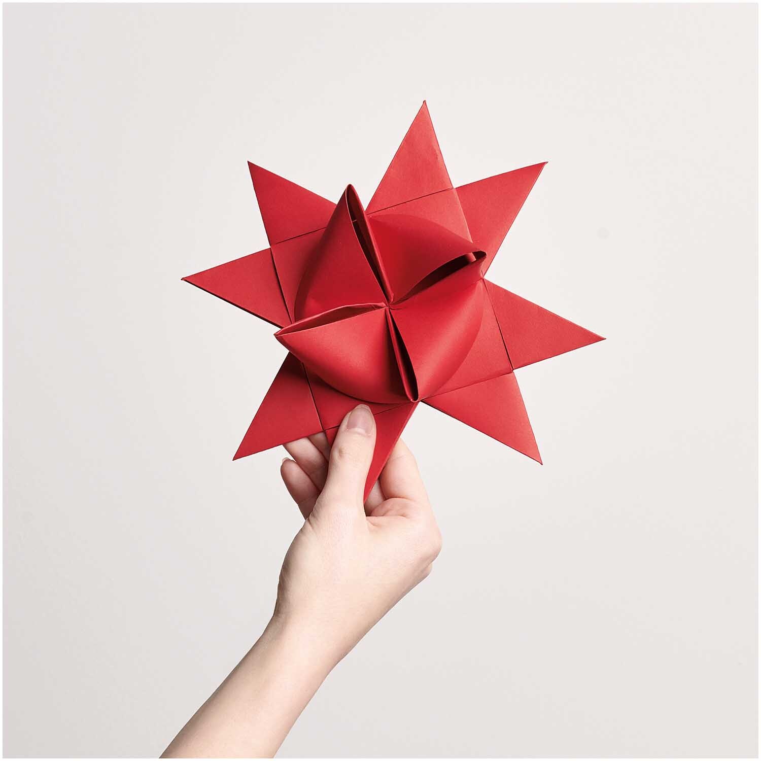 Paper Poetry Fröbelstreifen XXL 180g/m2 20 Stück: Hand hält roten Fröbelstern von Rico Design vor weißem Hintergrund.