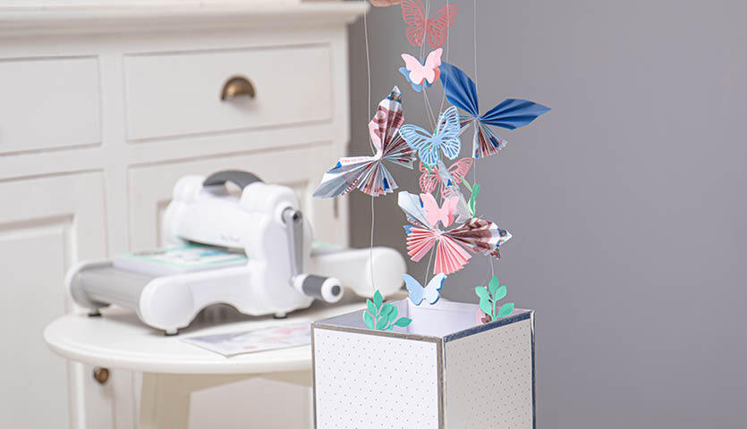 Bastelanleitung Geldgeschenk mit Schmetterlingen: Bunte Papier-Schmetterlinge schweben über einer dekorativen Box.